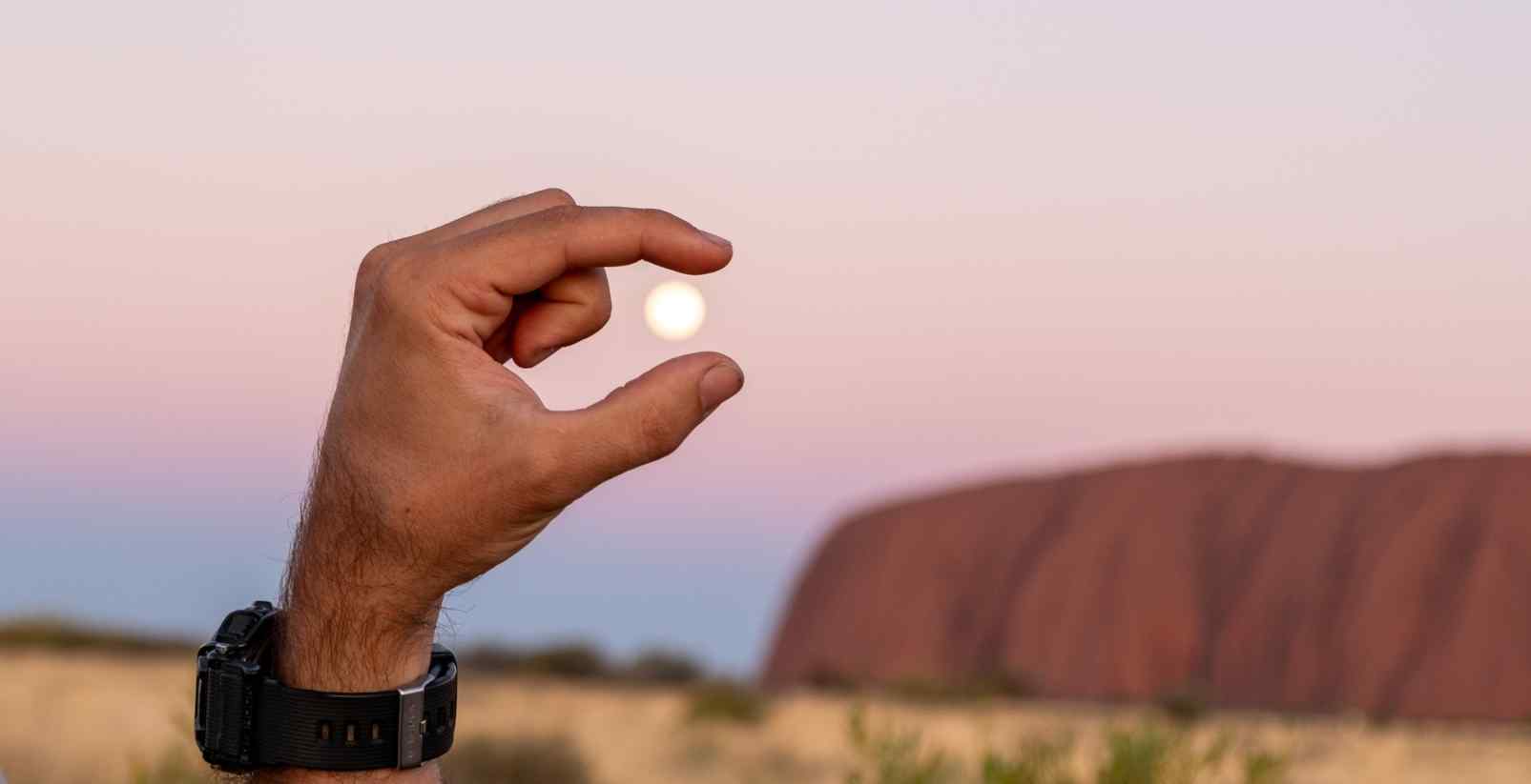 person pretending to hold moon between fingers