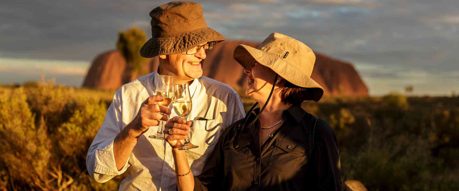 older Couple clinking winge glasses in front of Uluru