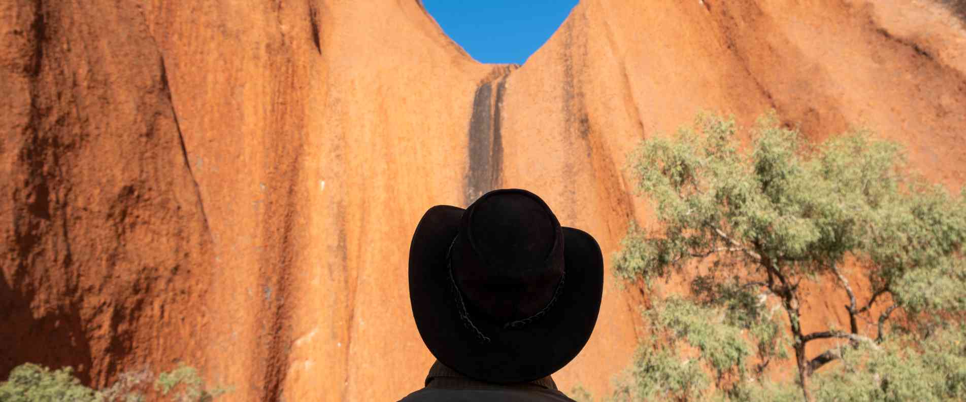 Man wearing Acubra hat facing towards uluru 